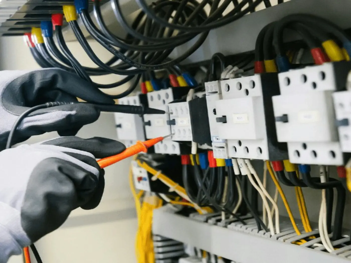 Eldivenli bir teknisyenin elektrik kontrol panosundaki bir kontaktörü multimetre problarıyla ölçmesi